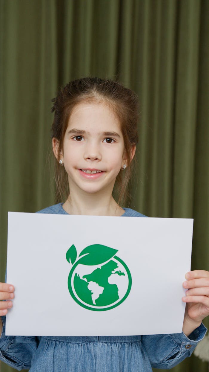 Crafting Captivating Headlines: Your awesome post title goes here Young girl in blue dress holding eco-friendly Earth symbol poster indoors.