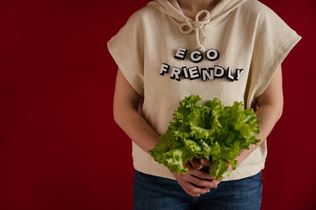 Woman in an eco-friendly hoodie holding fresh lettuce against a red background.
