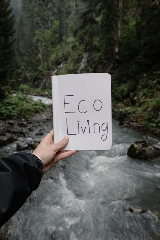 Hand holding a notebook with 'Eco Living' text against a scenic forest river backdrop.